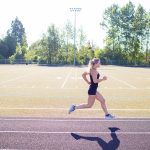 Female runner performs short sprints while working out on an outdoor track in the summer.