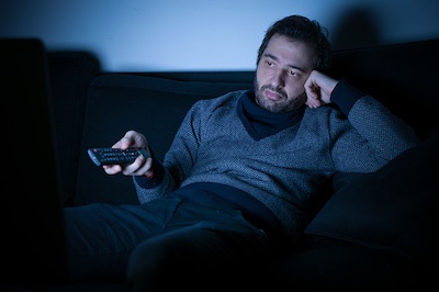 Bored man watching television at night lying on the couch