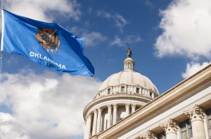 State Capitol Building in Oklahoma City with US state flag outside on a partly cloudy day